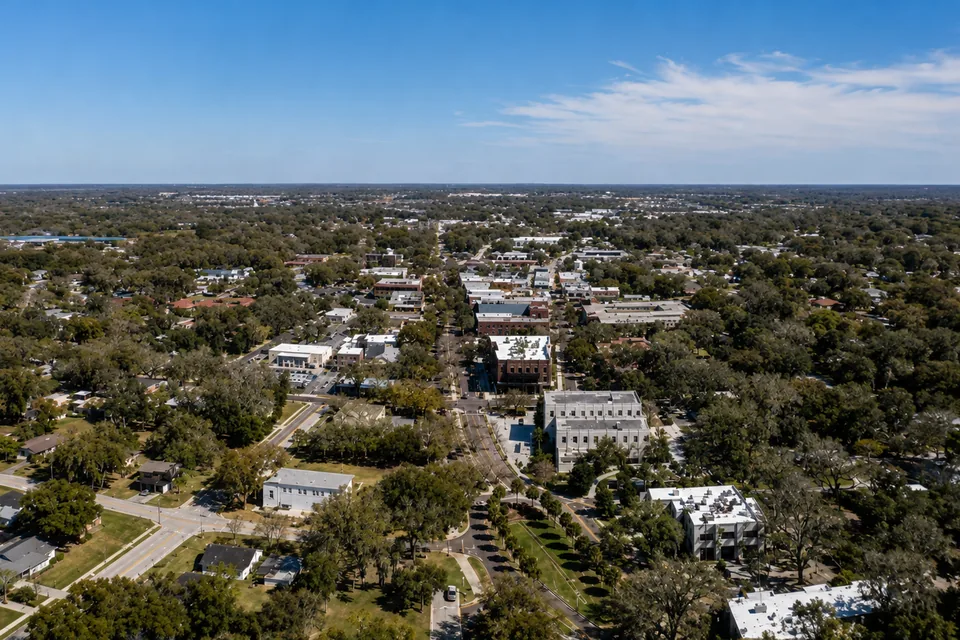A Central Florida downtown seen from the air, low-rise brick storefronts along a main street under mature oak canopy, representative of the Winter Garden area